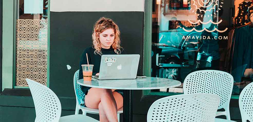 Local girl seen sitting at a table in front of Amavida's cafe in Rosemary Beach FL with a cold brew coffee and her laptop.