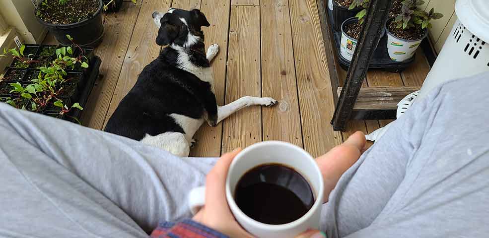 Jennifer sitting on her porch enjoying a cup of coffee with her pup Brock.